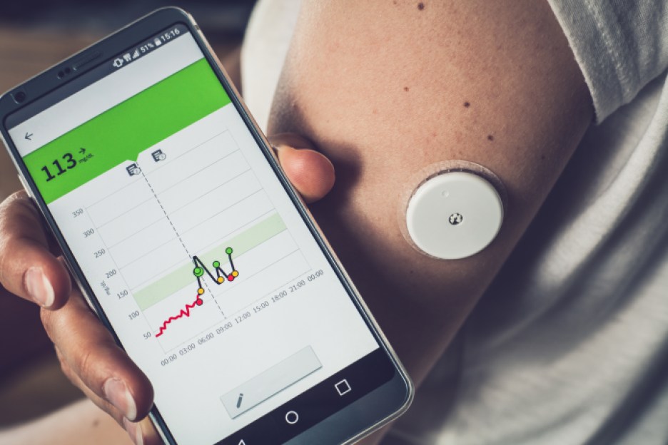 Woman checking glucose level with a remote sensor and mobile phone for diabetes treatment.